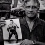 Eddie Sharkey, older, holds photo of his younger self in wrestling trunks.